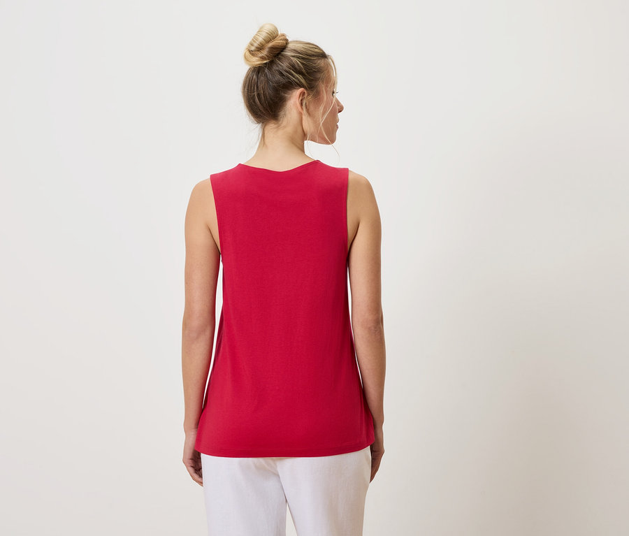 Pohled zezadu na ženu s drdolem, oblečenou v červeném tílku a bílých kalhotách.