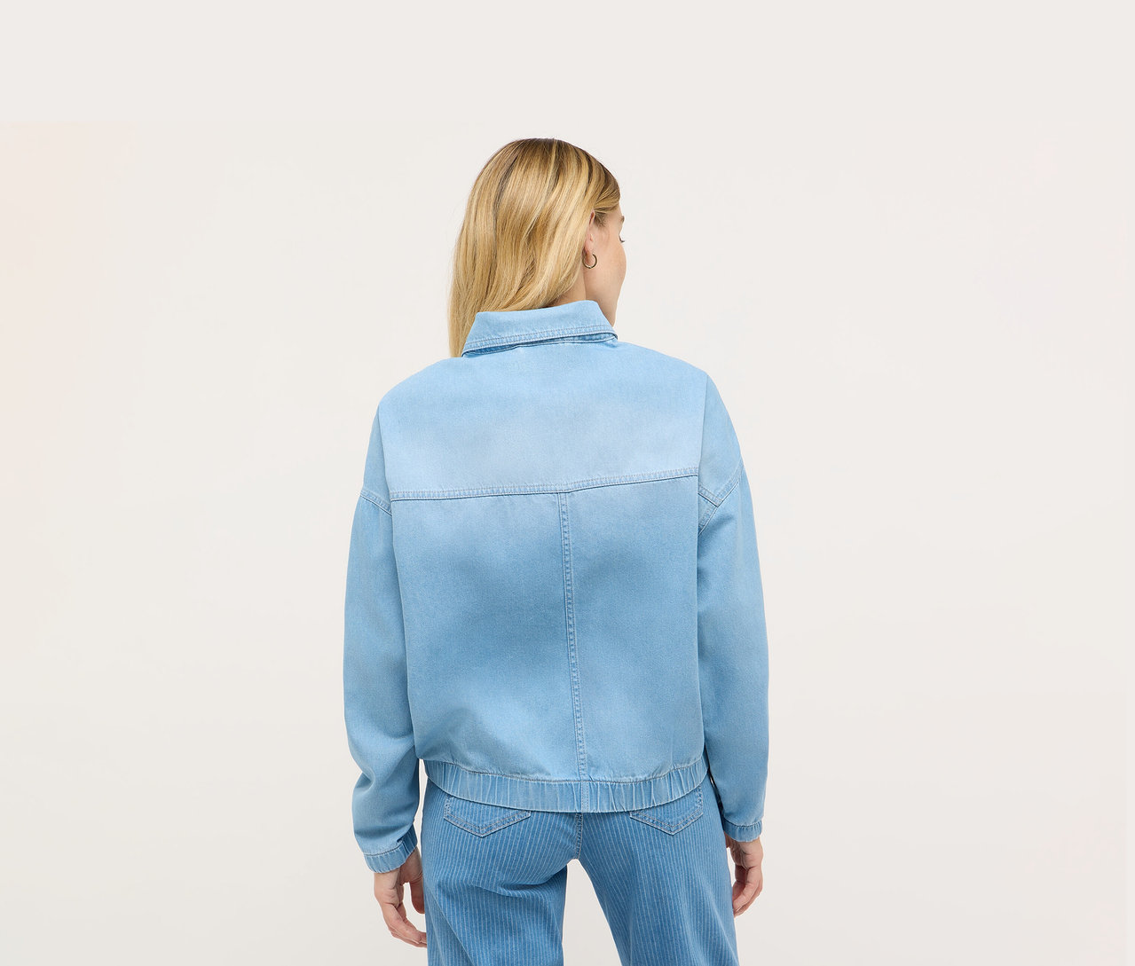 Pohled zezadu na blondýnu v modré džínové bundě Angels.