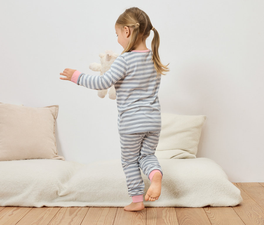 Dívka v šedo-bílém pruhovaném pyžamu drží plyšového medvěda na gauči.