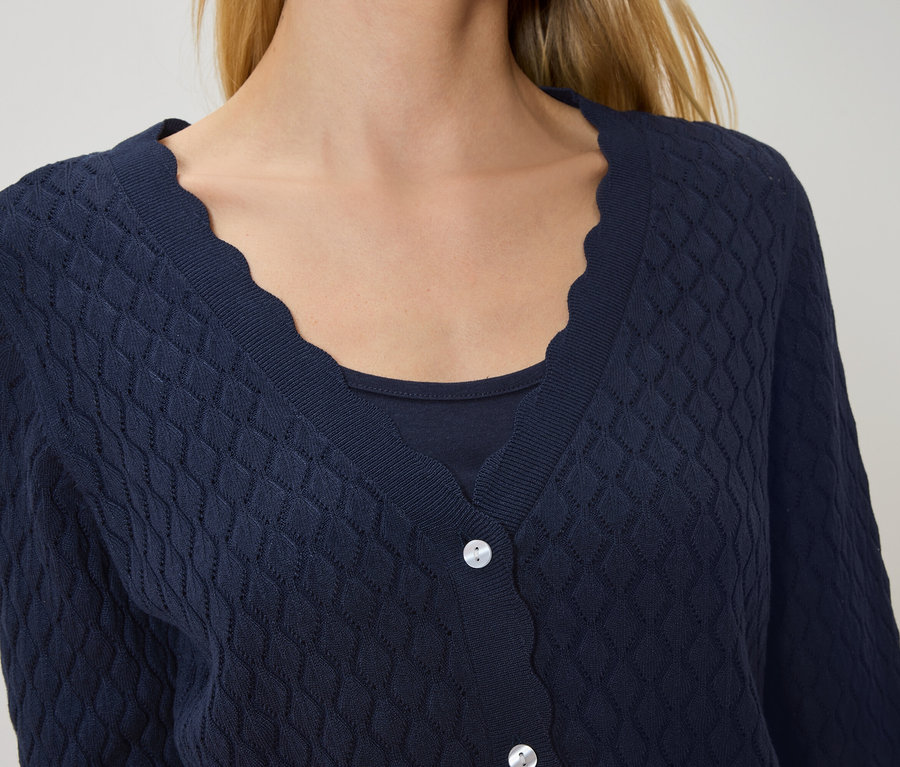 Žena má na sobě tmavě modrý kardigan se zvlněným lemem přes tmavě modrý top.