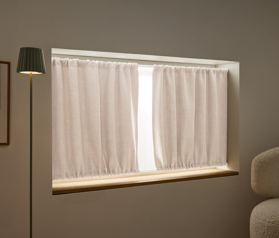 Pohled na okno s béžovými závěsy, zelenou stojací lampu a abstraktní umělecké dílo na stěně.