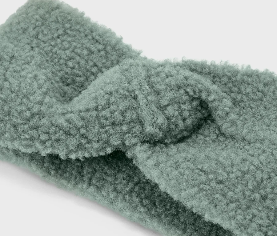 Detailní záběr světle zelené, zkroucené čelenky z plyše teddy.