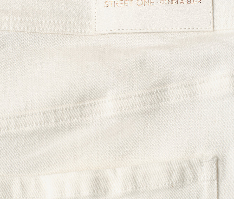 Detail bílých Džíny Street One s bledou etiketou s textem 'designed with passion STREET ONE - DENIM ATELIER'.