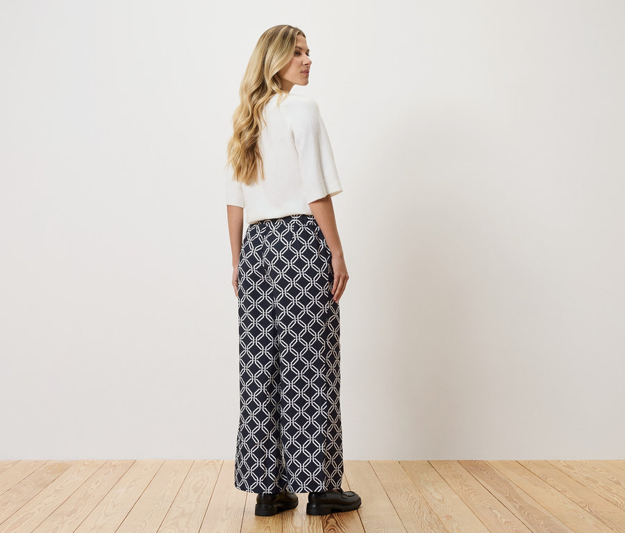 Žena má na sobě bílý top a dlouhé, tmavě modré kalhoty s bílým geometrickým vzorem.