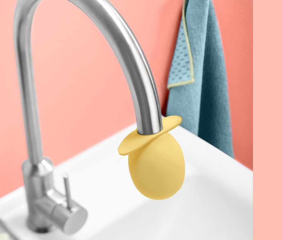 Žlutý nástavec na odvápnění vodovodního kohoutku na stříbrném kohoutku v bílém umyvadle.