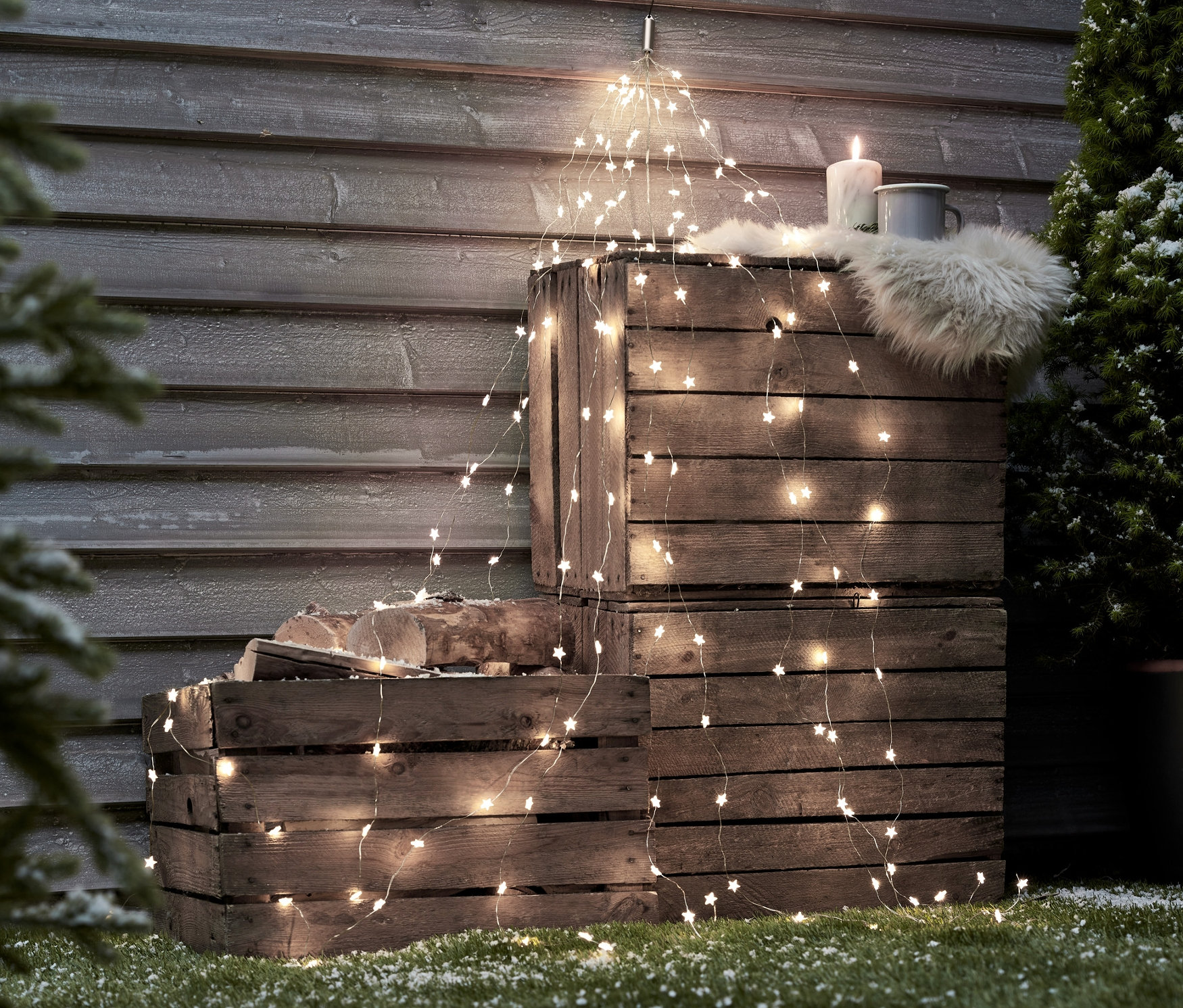 Dřevěné bedny naskládané na sobě, ozdobené LED světelnými řetězy, svíčkou, kožešinou a hrnkem.