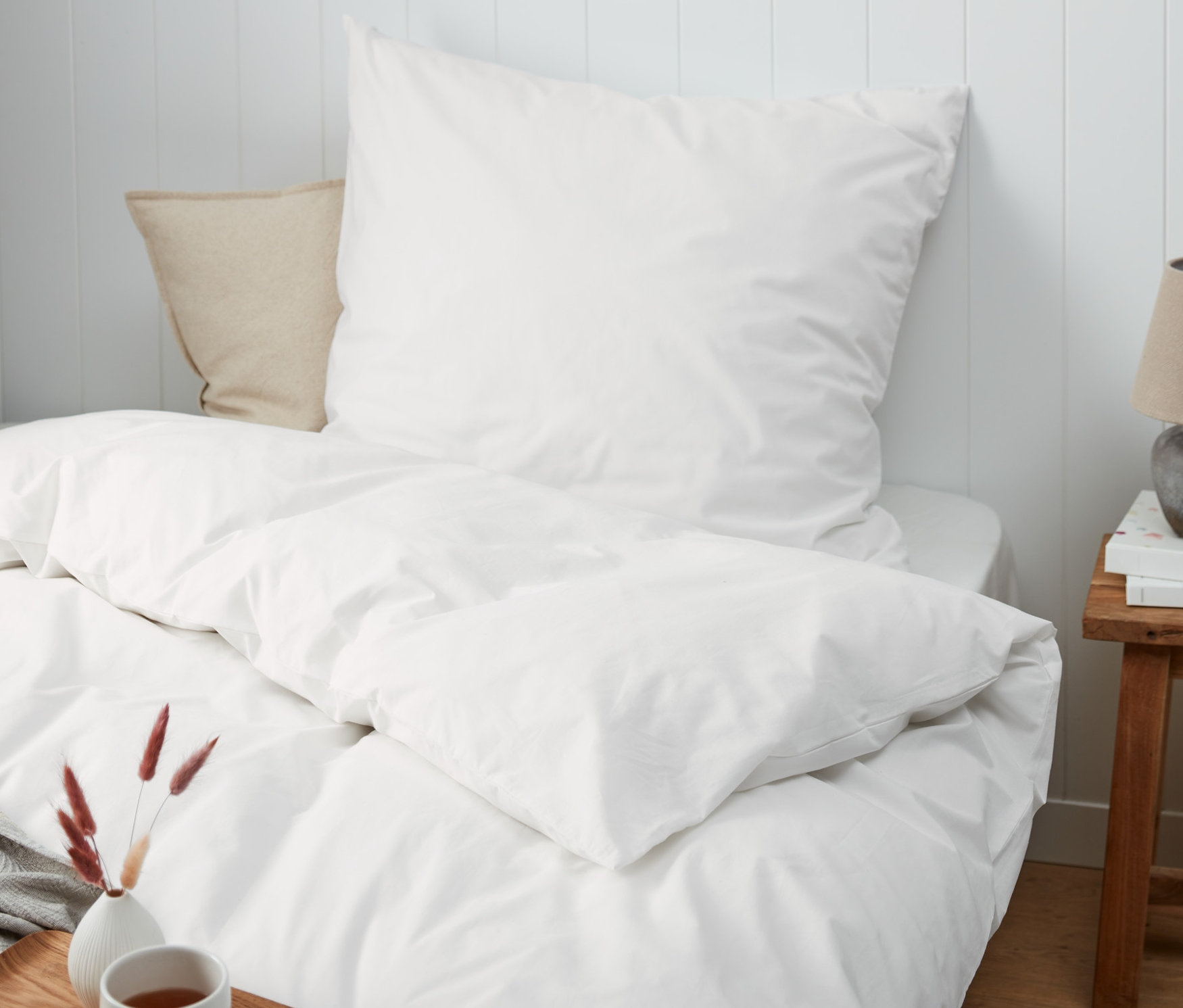 Bílé perkálové povlečení standardní a nadměrné velikosti na posteli s dřevěným podnosem, šálkem a vázou.