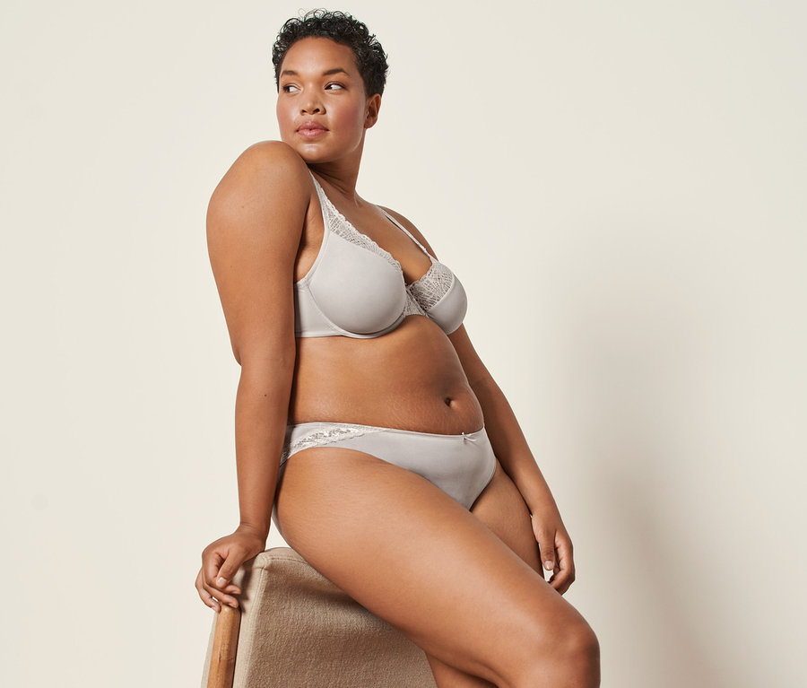 Žena sedí na židli a má na sobě mandlové kalhotky (2 ks) a podprsenku s kosticemi.