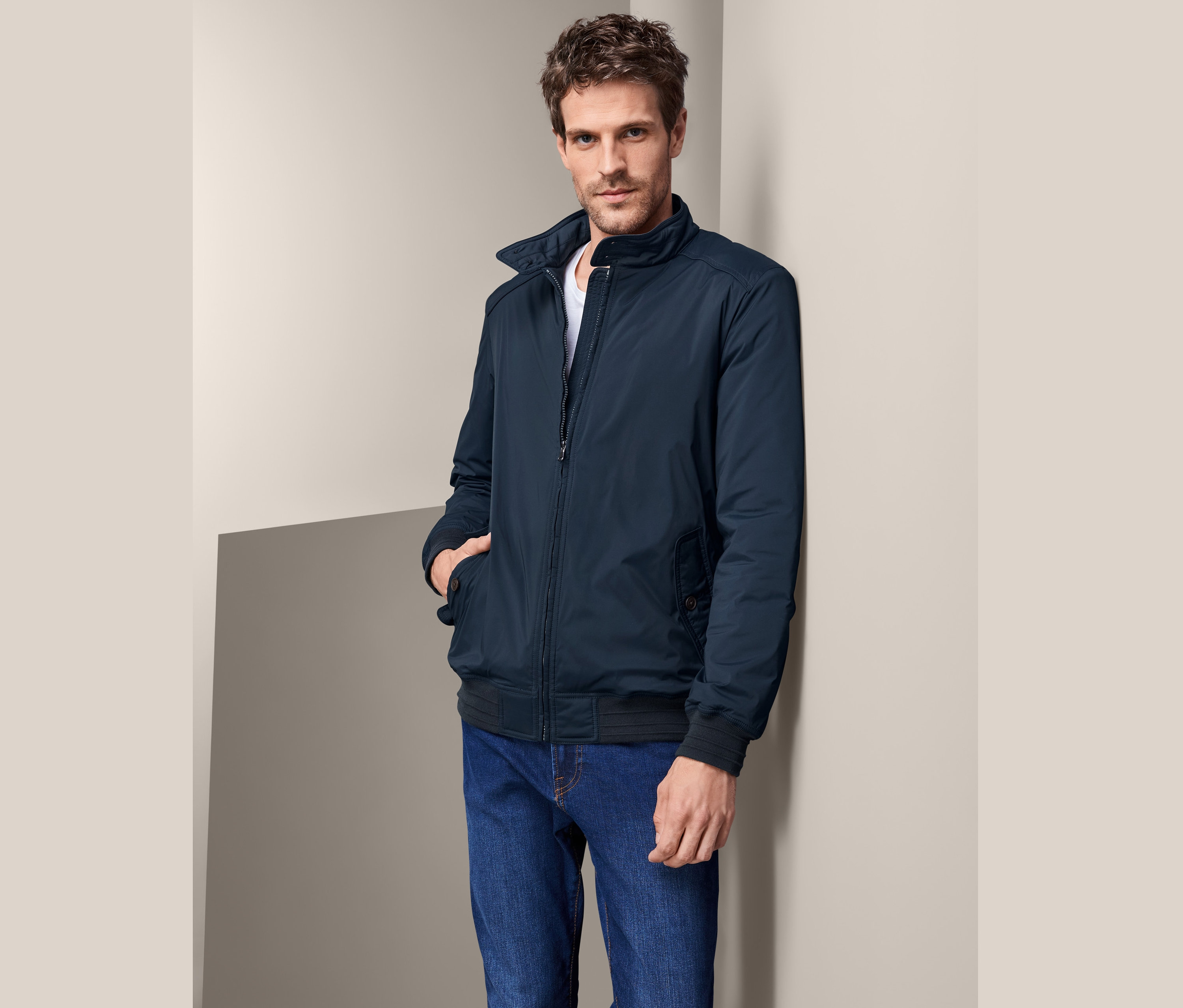 Muž opřený o zeď má na sobě modrý bluzon a džíny.