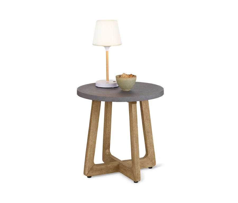 Na kulatém odkládacím stolku s betonovou deskou stojí lampa a miska s jídlem.