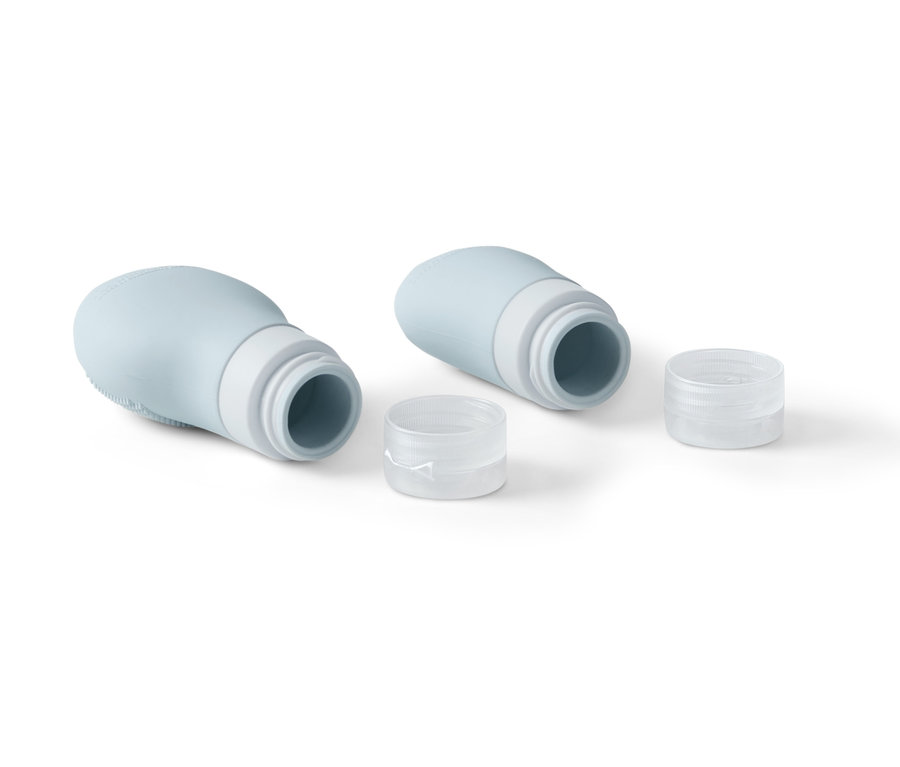 Dvě světle modré lahvičky na šampon s průhlednými víčky leží na bílém pozadí.