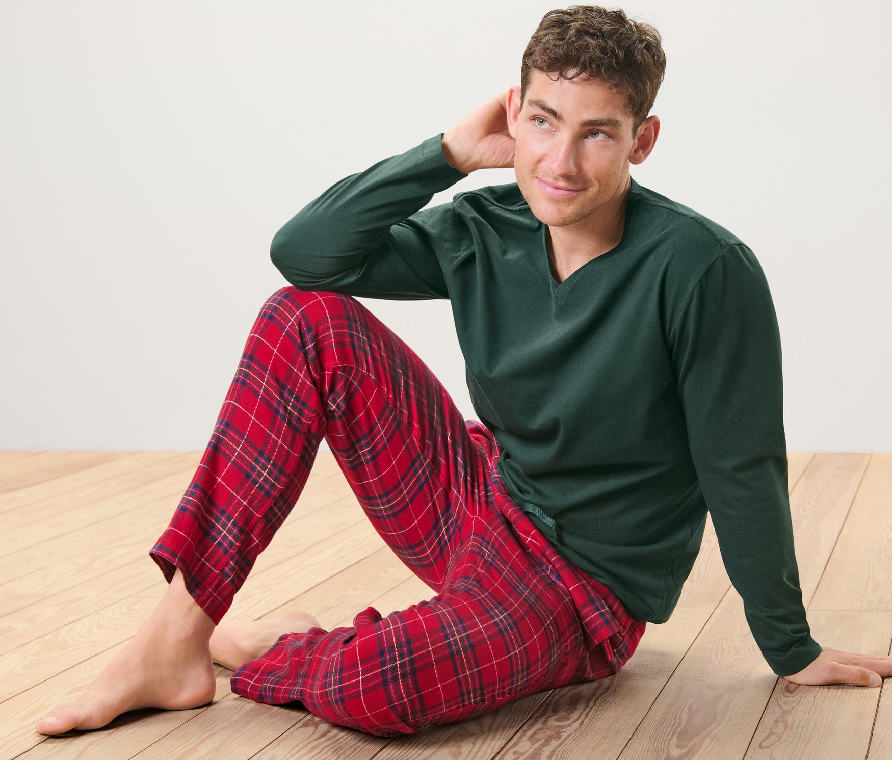 Muž sedí na podlaze a má na sobě zelené pyžamo s flanelovými kalhotami červené barvy.