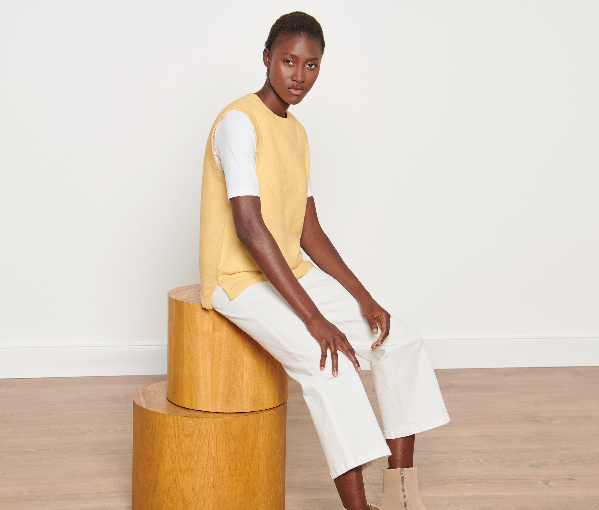 Žena sedí na dřevěných stoličkách a má na sobě pletenou vestu přes hlavu.