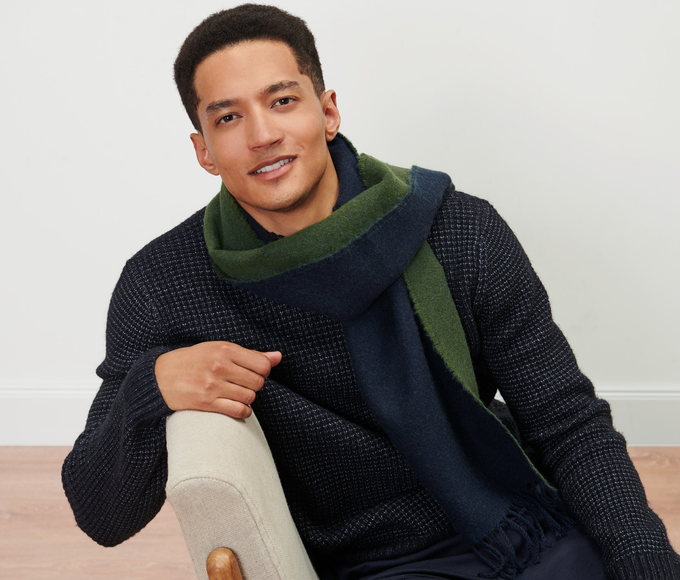 Muž sedí na židli a má na sobě tkanou šálu.