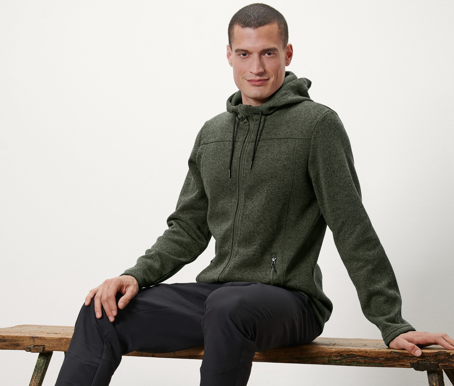 Muž sedí na lavičce a má na sobě bundu z pleteného fleecu.