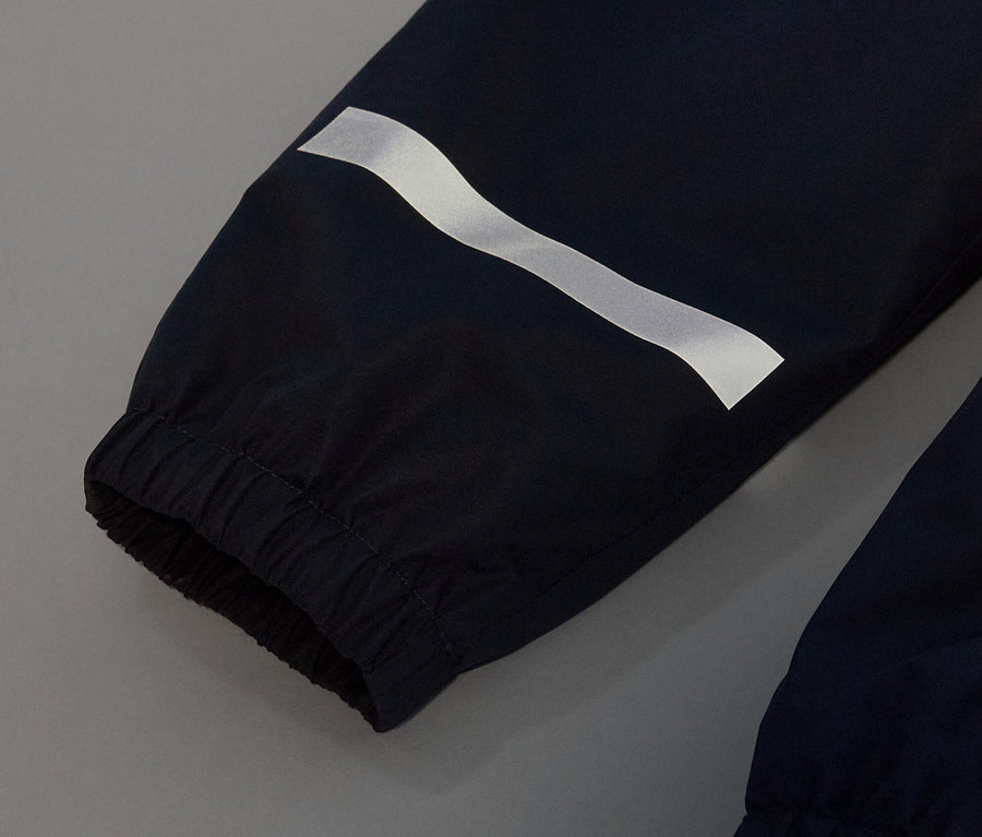 Detail dětských kalhot do deště tmavě modré barvy s reflexním pruhem.