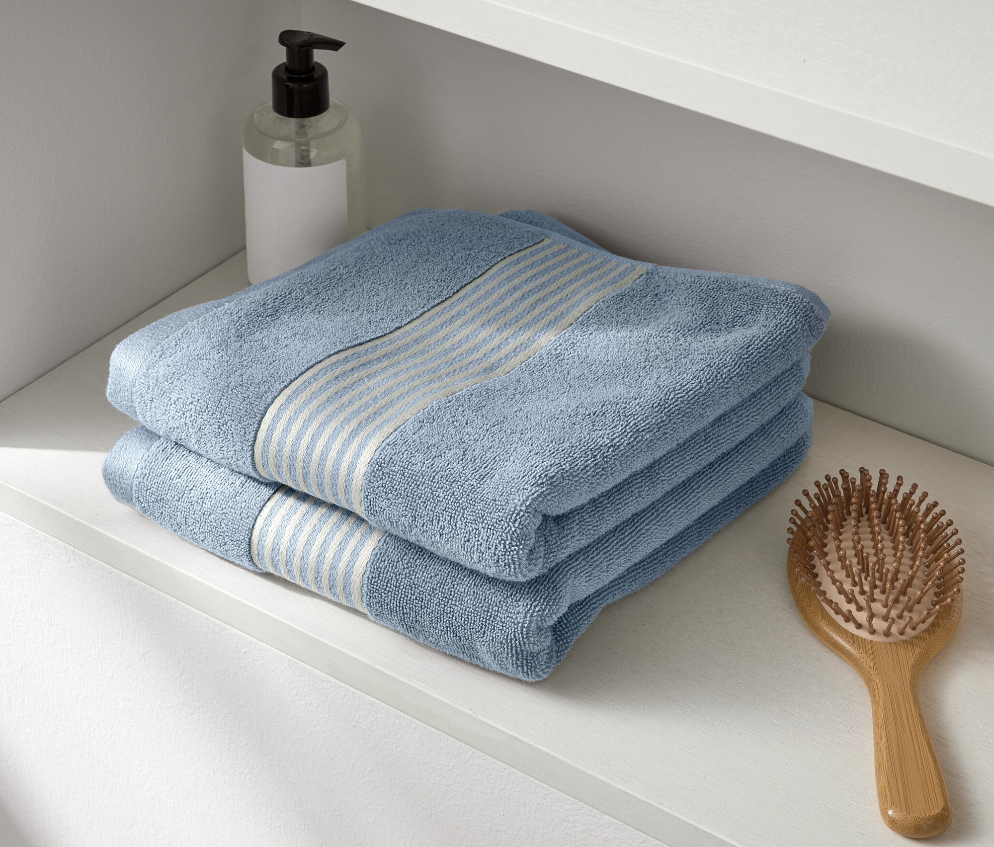 Na bílé polici leží dva modré prémiové ručníky.
