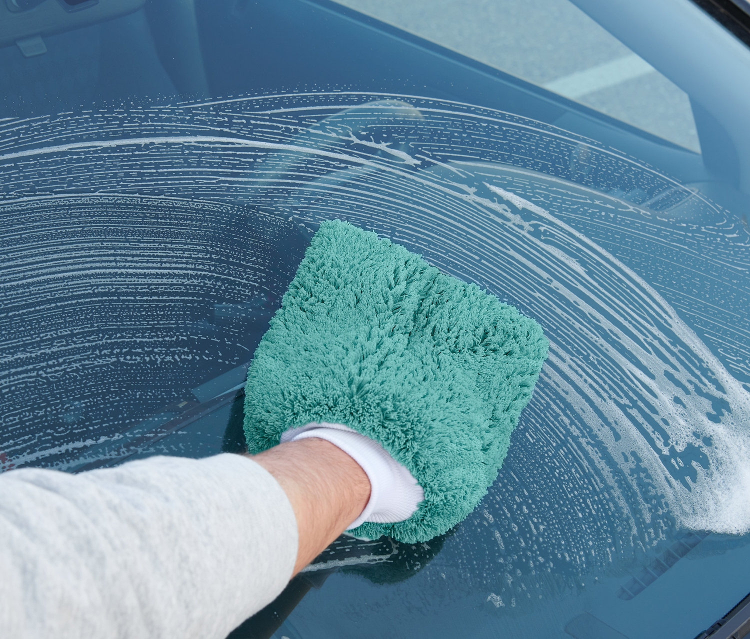 Muž umývá čelní sklo auta pomocí mycí rukavice na auto.