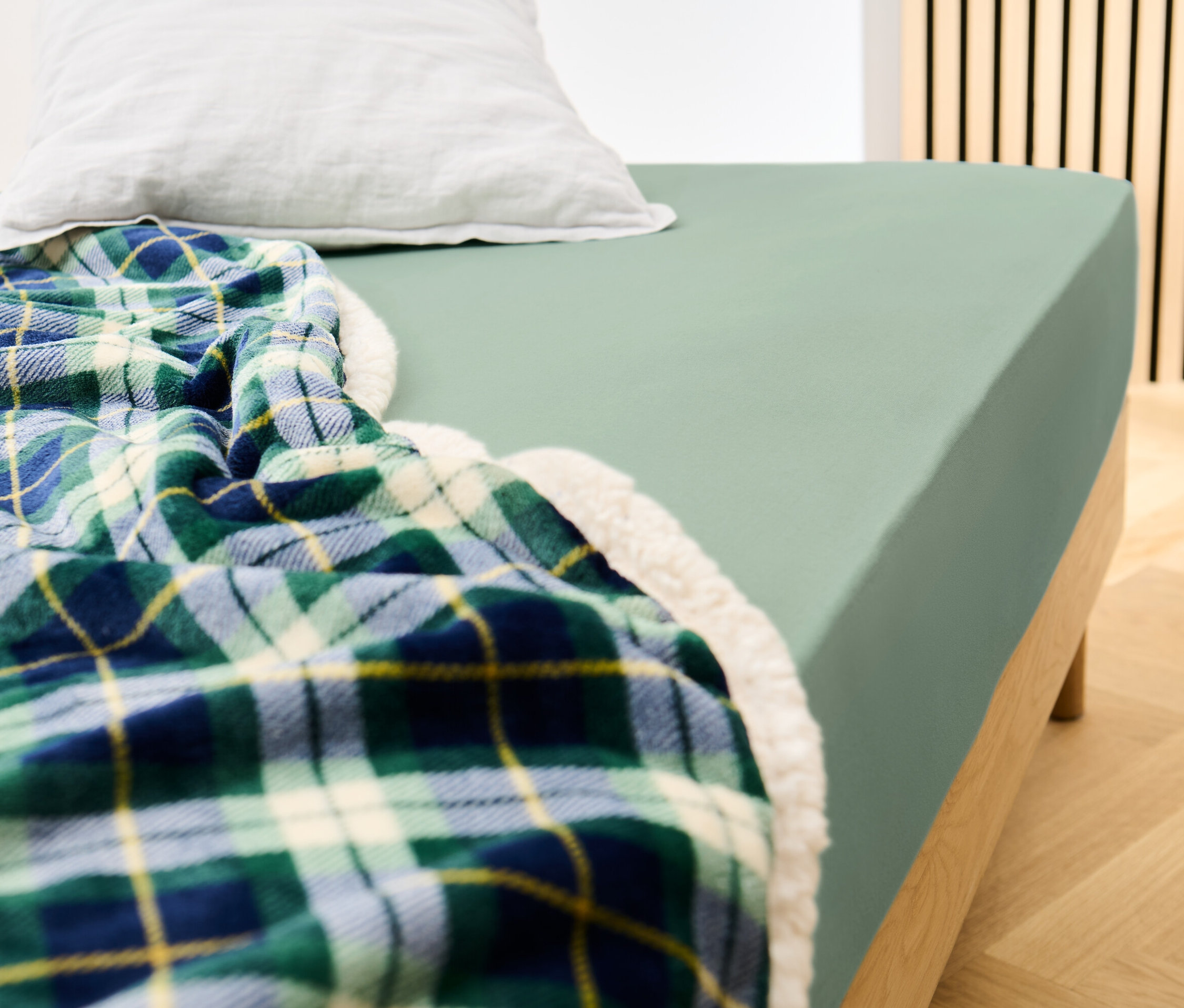 Postel s prostěradlem šalvějové barvy a kostkovanou dekou.