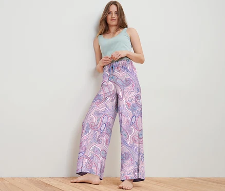 Žena pózuje ve studiu a má na sobě tkané kalhoty s paisley vzorem a světle zelený top.