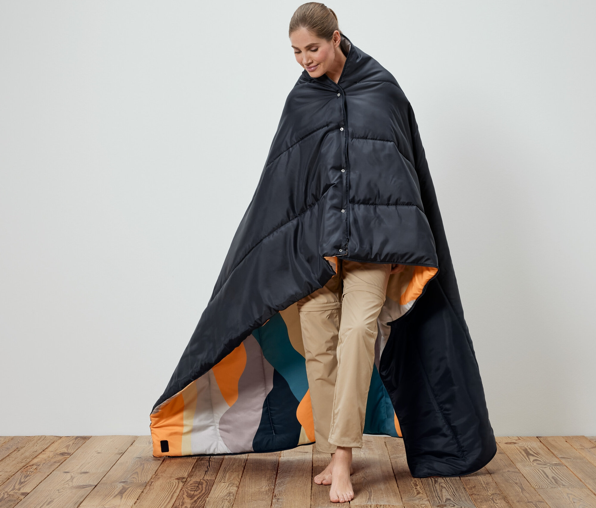 Žena zahalená do černého dekového spacího pytle 4 v 1. Vnitřek spacího pytle je vzorovaný.