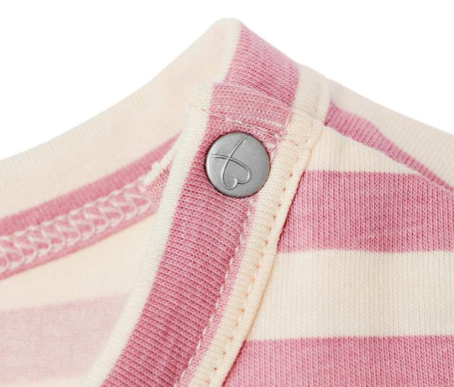 Detail žerzejových šatů pro miminka s růžovými a krémovými pruhy a stříbrným knoflíkem ve tvaru srdce.