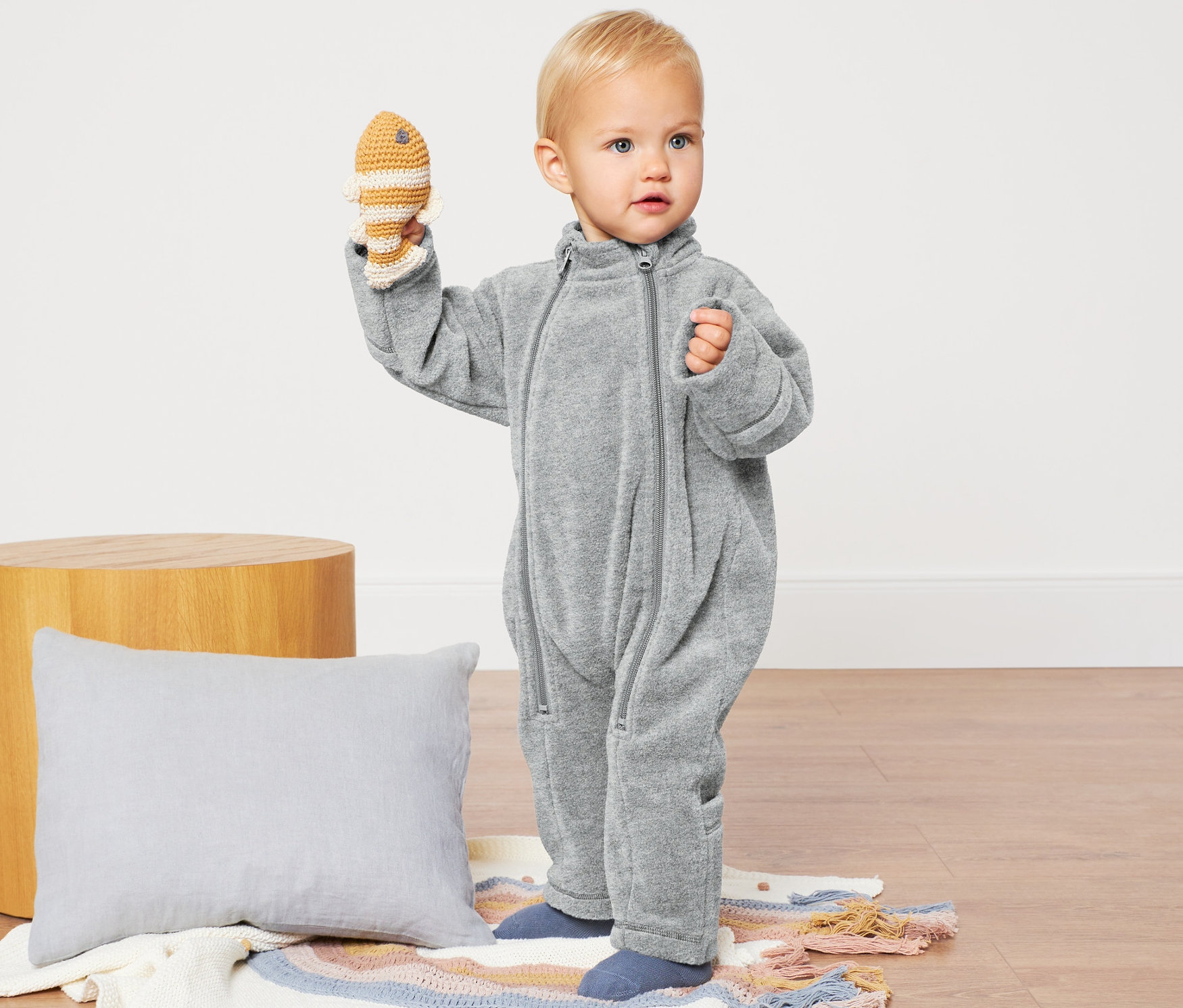 Batole drží háčkovanou rybu, má na sobě šedý fleecový overal.