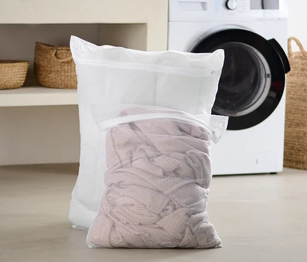 Dvě extra velké síťky na praní prádla stojí na podlaze v koupelně před pračkou.