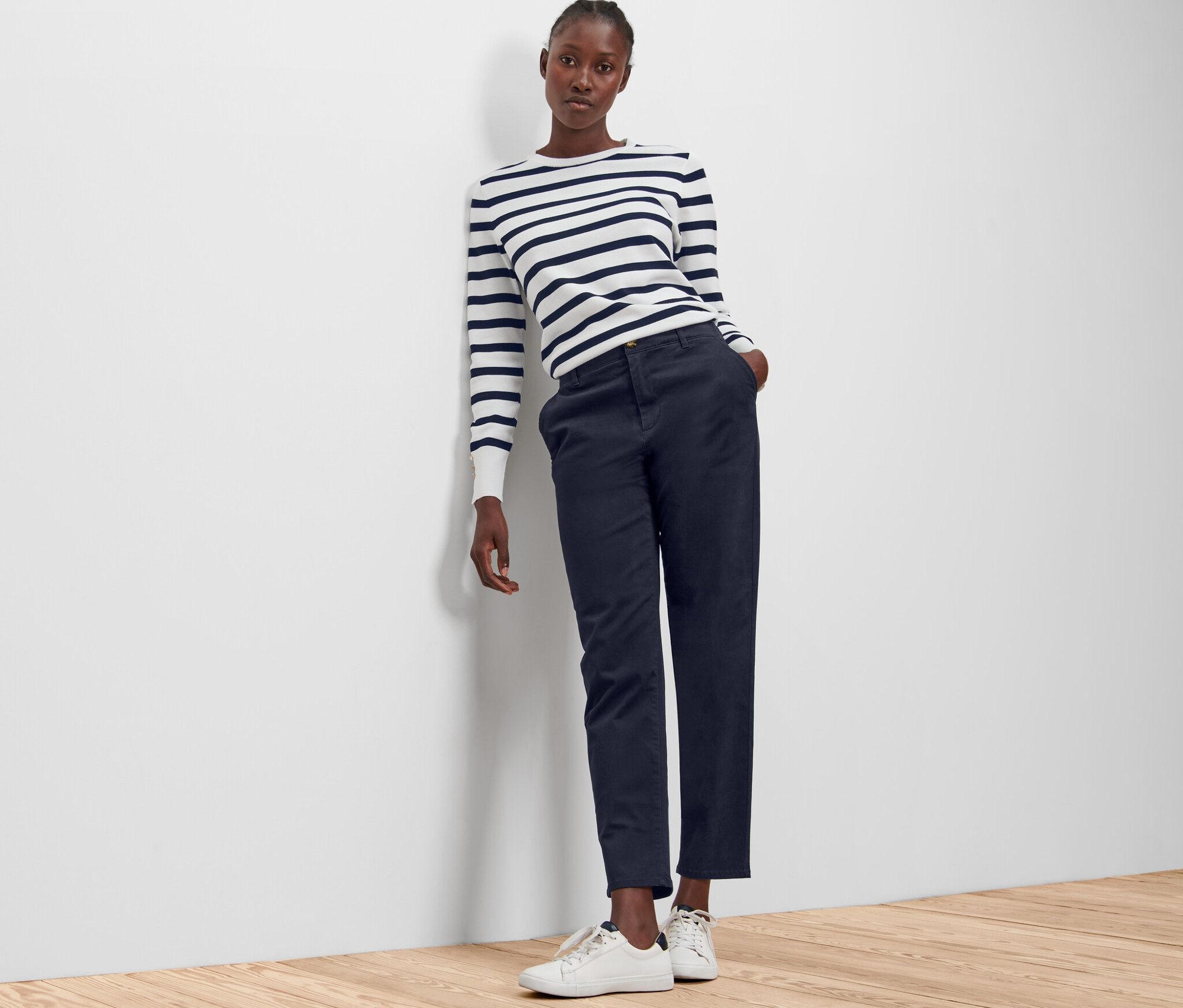 Žena opřená o zeď má na sobě tmavě modré chino kalhoty.