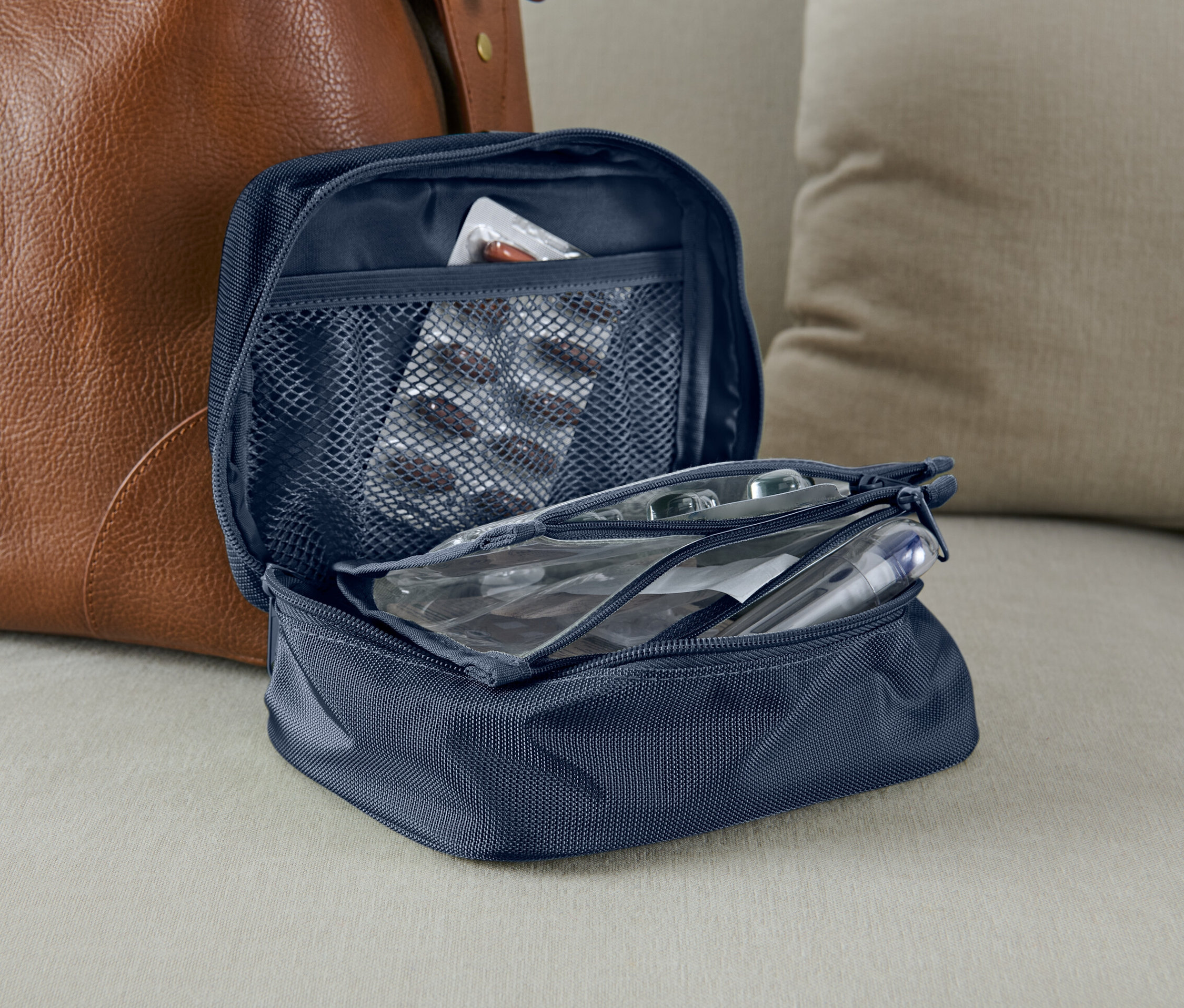 Otevřená modrá taška na léky vedle hnědé kožené tašky.