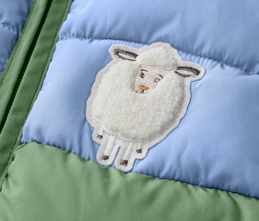 Detail dětské prošívané vesty s color blockingem a nášivkou ovečky.