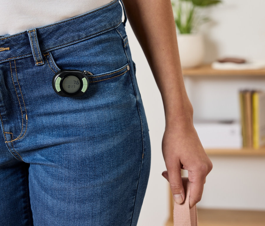 Černý krokoměr připevněný k přední kapse modrých džínů.