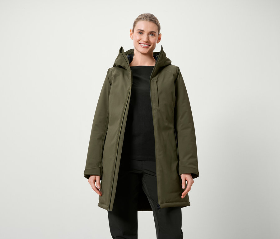 Žena pózuje v olivově zelené bundě s kapucí a černém oblečení.