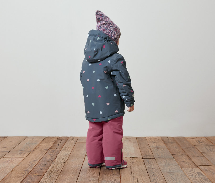 Zezadu je vidět dítě v zimní bundě s kapucí se vzorem srdíček a v růžových oteplovákách.