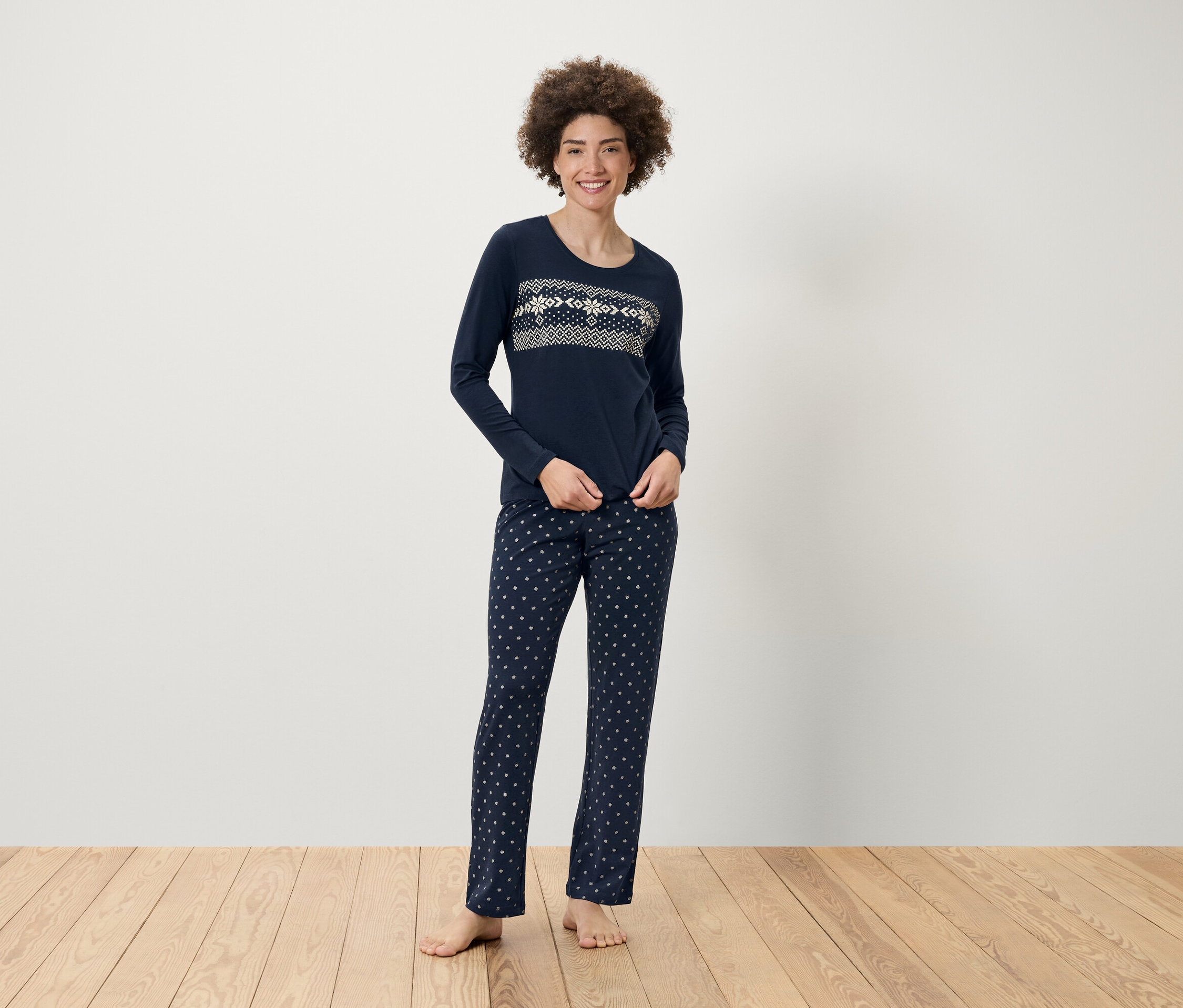 Žena stojí a má na sobě tmavě modré pyžamo s dlouhým rukávem a vzorem.