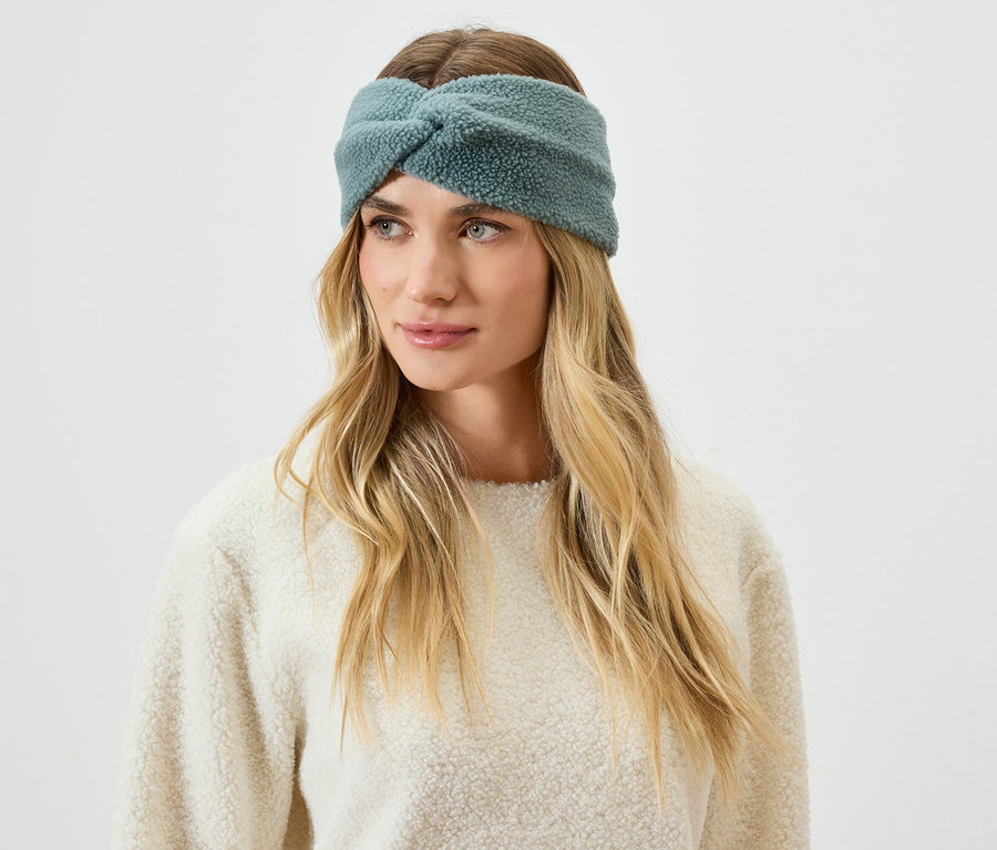 Portrét ženy s blond vlasy a modrozelenou chlupatou čelenkou.