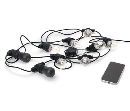Černý venkovní světelný řetěz s LED a 2 reproduktory Bluetooth® leží vedle mobilního telefonu na bílém pozadí.