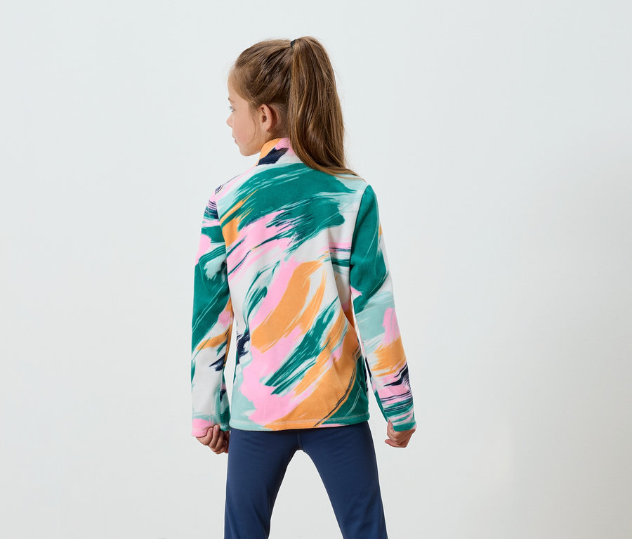 Dívka s hnědými vlasy v culíku stojí zády a má na sobě mikinu se vzorem tahů štětce v zelené, růžové a oranžové barvě a modré kalhoty.