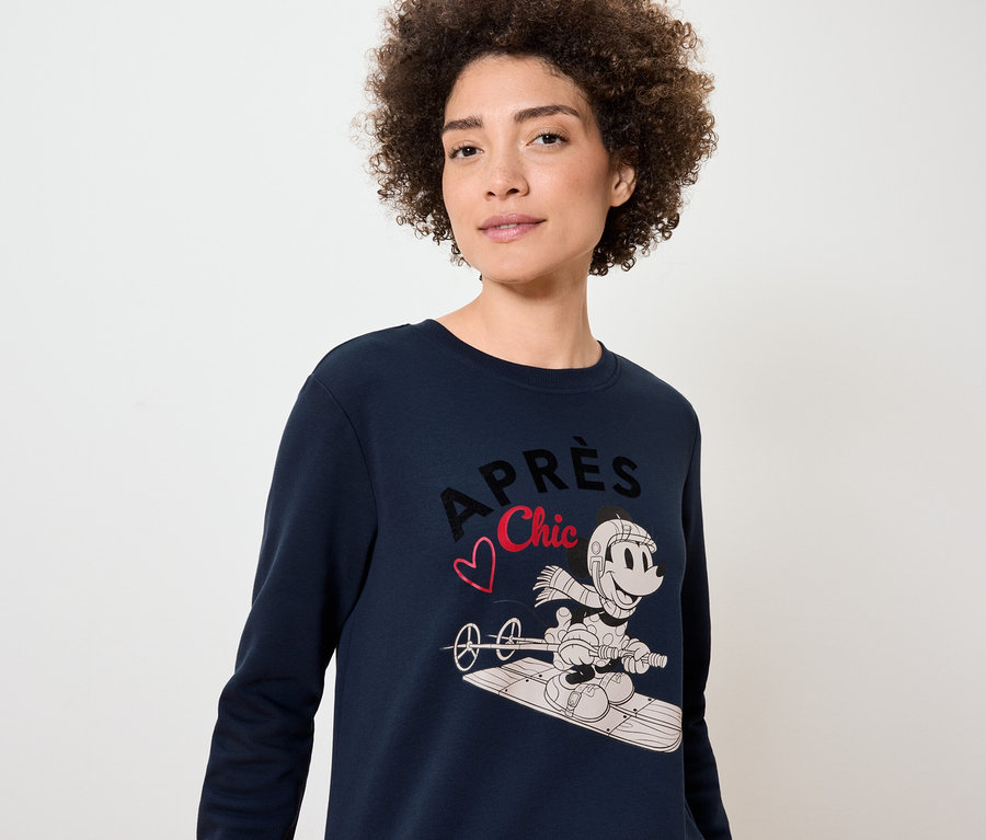 Žena má na sobě tmavě modrý svetr s potiskem Mickey Mouse na snowboardu.