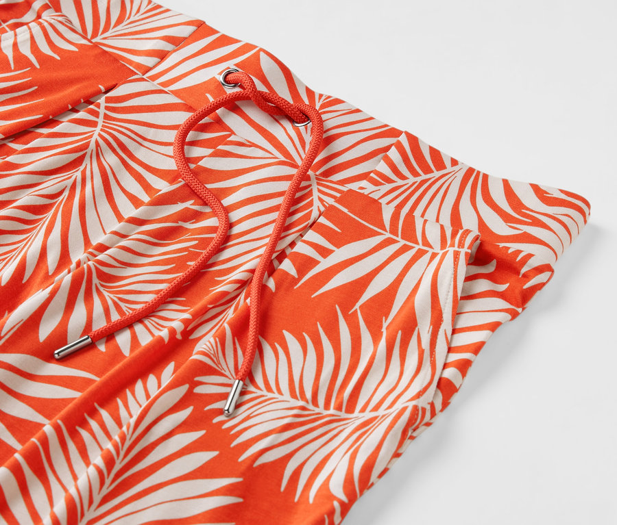 Detail oranžových jersey kalhot s potiskem listů a oranžovou stahovací šňůrkou.