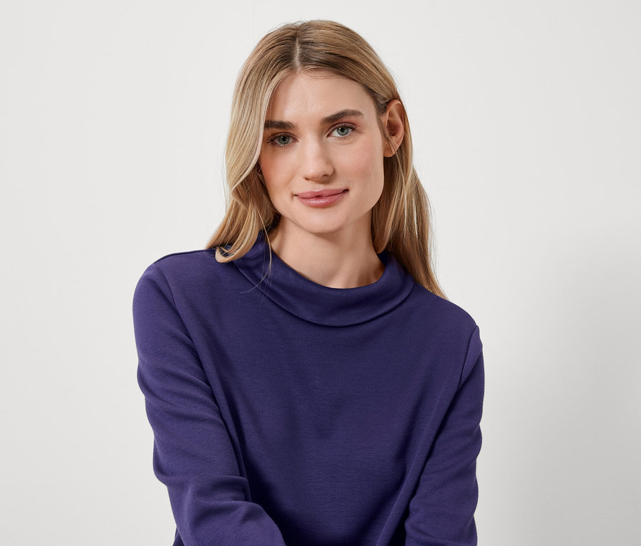 Portrét ženy s blond vlasy v modrém roláku.