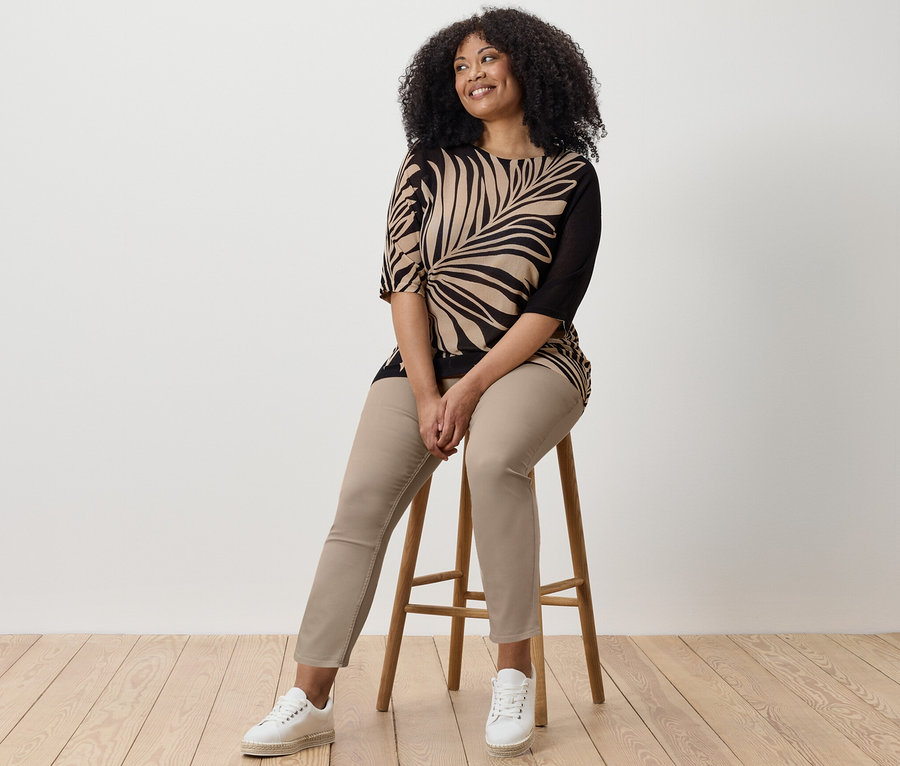 Žena sedí na stoličce a má na sobě 7/8 tregíny, top s potiskem a tenisky.