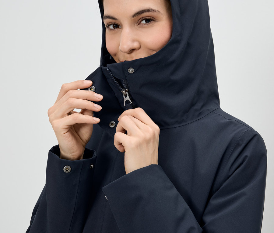 Žena si zapíná zip na tmavě modré bundě s kapucí.
