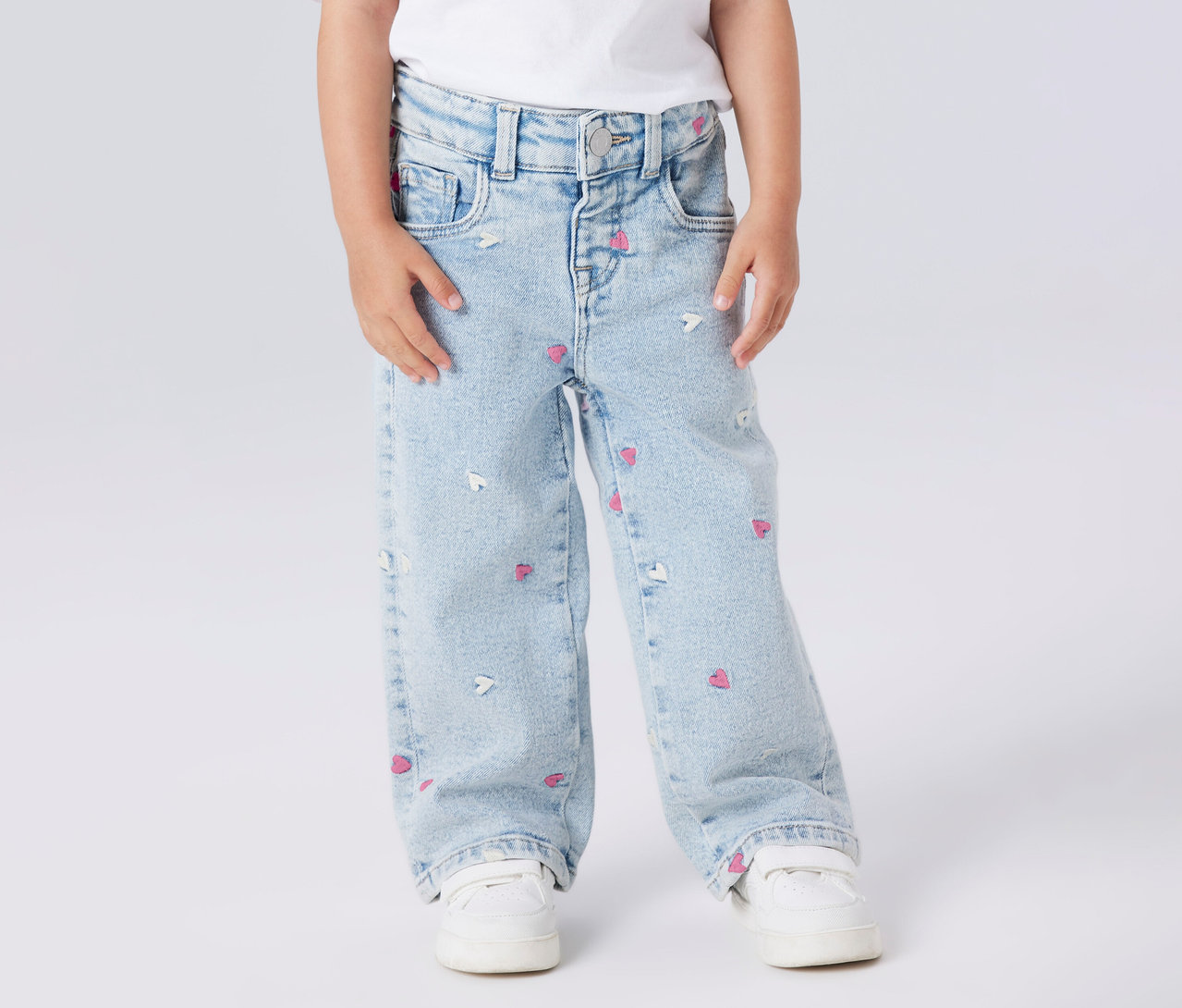 Dítě nosí džíny Dětské džíny wide leg NAME IT se vzorem srdce a bílé boty.