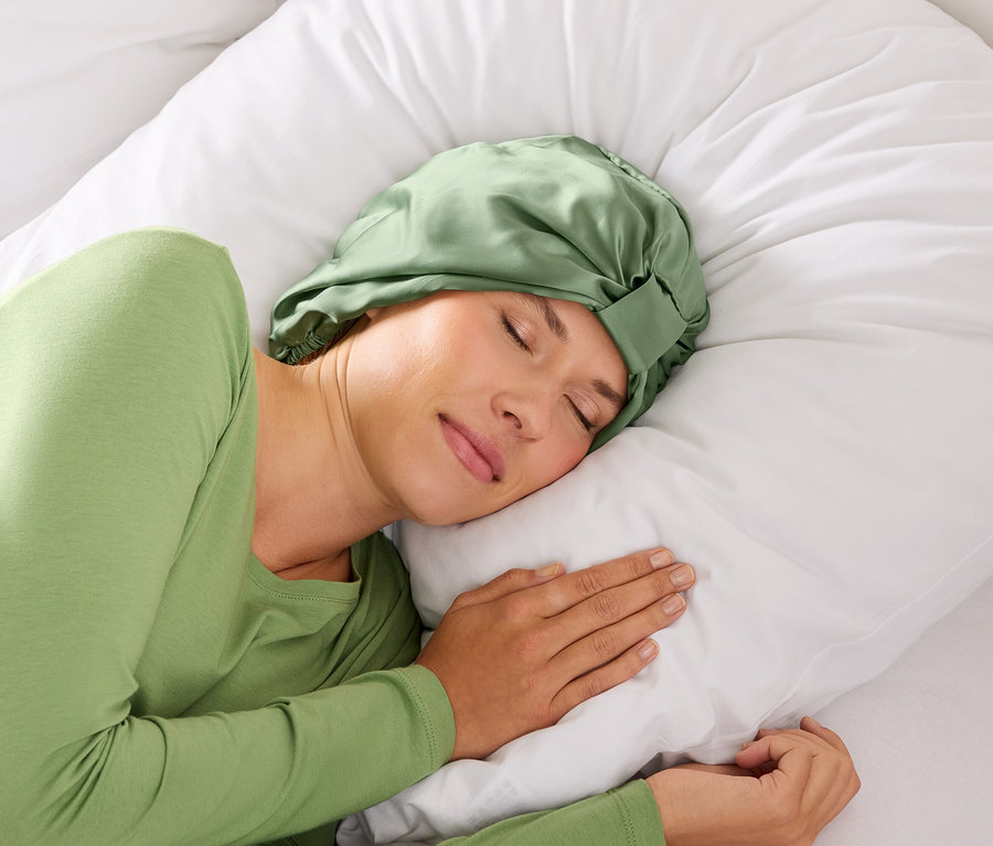 Žena spí se zelenou čelenkou na bílém polštáři.