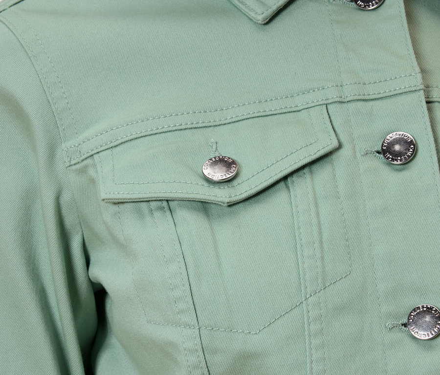 Detail světle zelené bundy se stříbrnými knoflíky a náprsní kapsou.