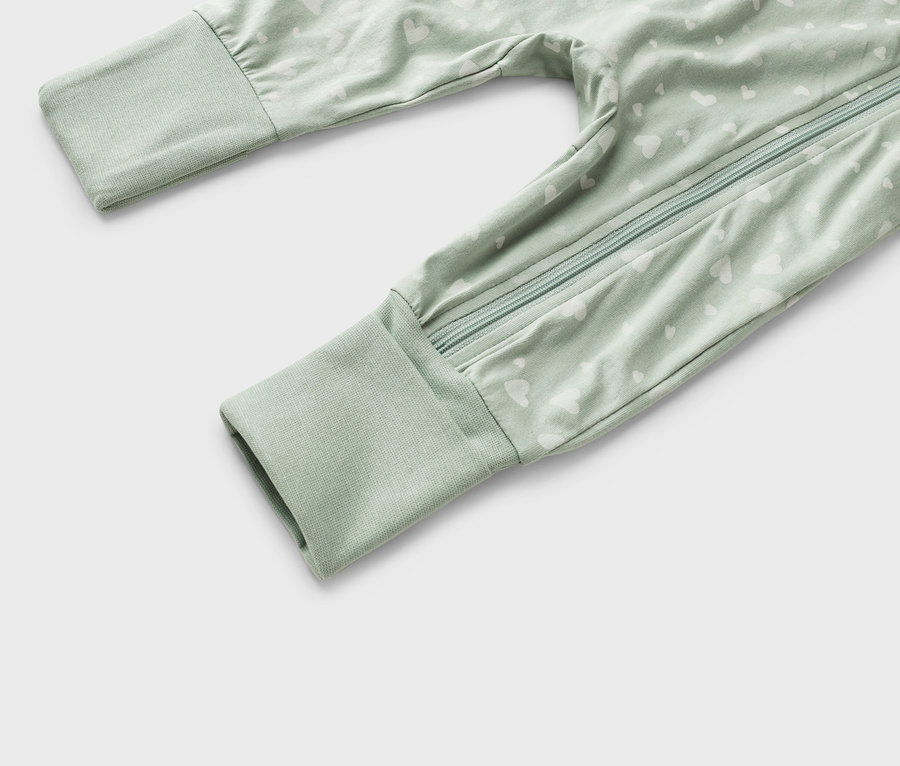 Detailní záběr na světle zelené dětské pyžamo s bílým vzorem srdce a zipem po celé délce.