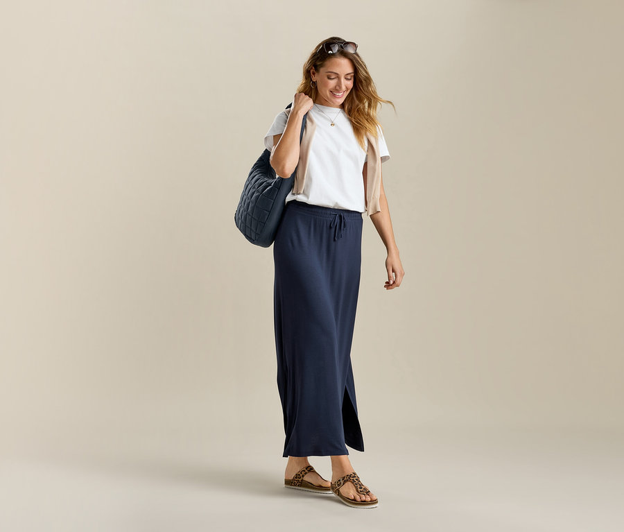 Žena v bílém tričku basic a dlouhé sukni Langer Jerseyrock. Má tašku přes rameno.