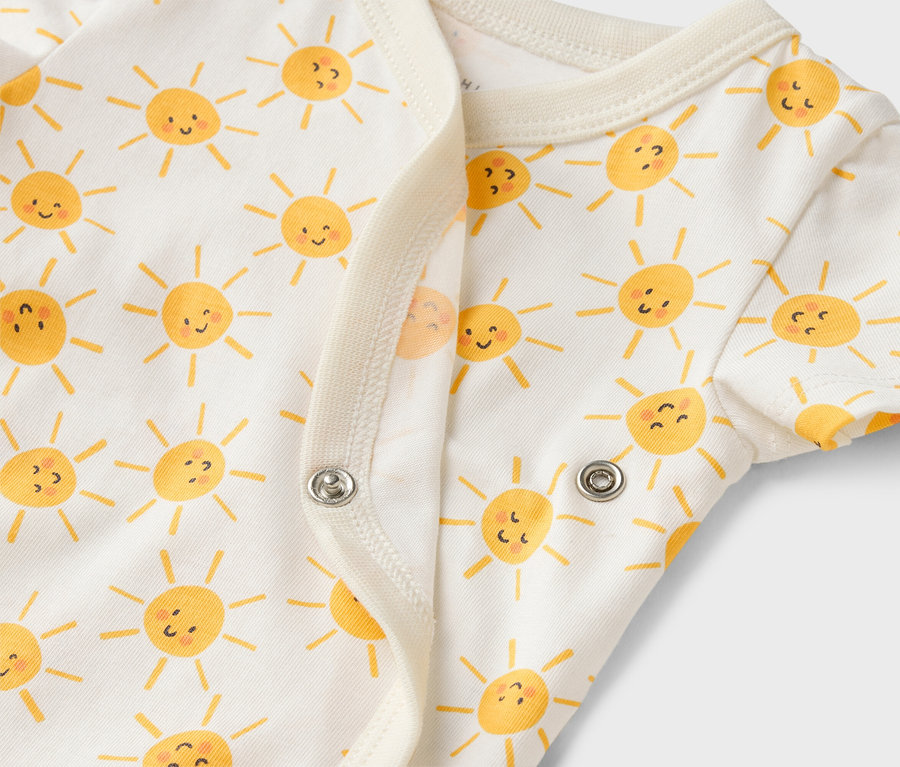 Detail bílého dětského body s potiskem žlutých sluníček a patentkami.