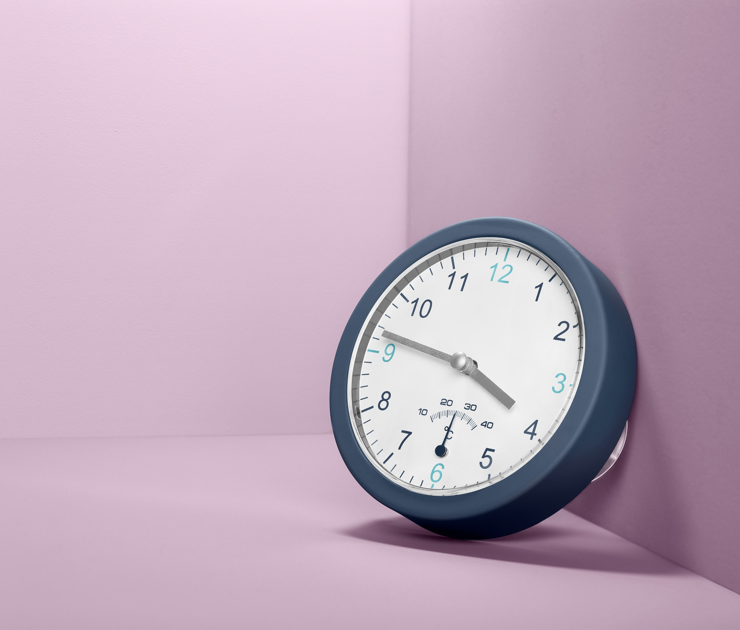 Modré nástěnné hodiny do koupelny s teploměrem na fialové zdi.